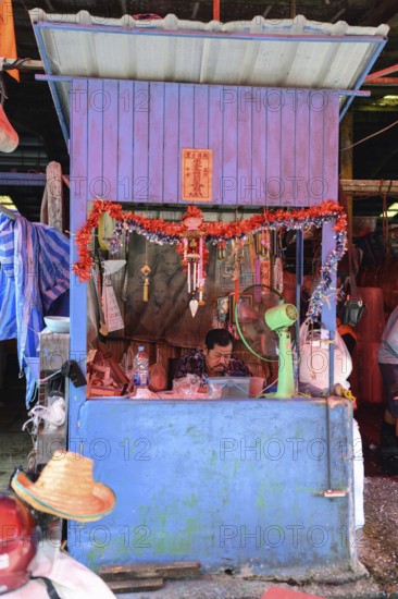 Bangkok, Thailand. February 19th 2025. A worker sits inside a colourful booth at the Khlong Toei