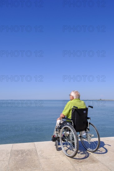 Senior in wheelchair looking at the sea, vacation with a handicap, Grado, Julian-Friuli, Adriatic