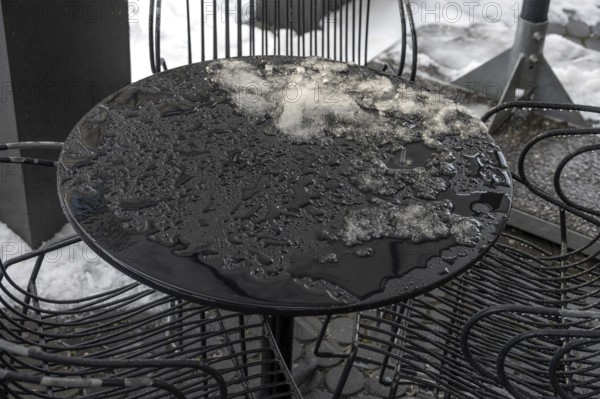 Thaw, remnants of snow on a bistro table outside during thaw in front of a café, Bavaria, Germany