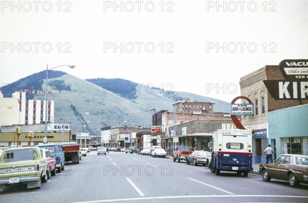 Vehicles on road Main Street in town downtown shopping area of Missoula, Montana, USA 1977 view to