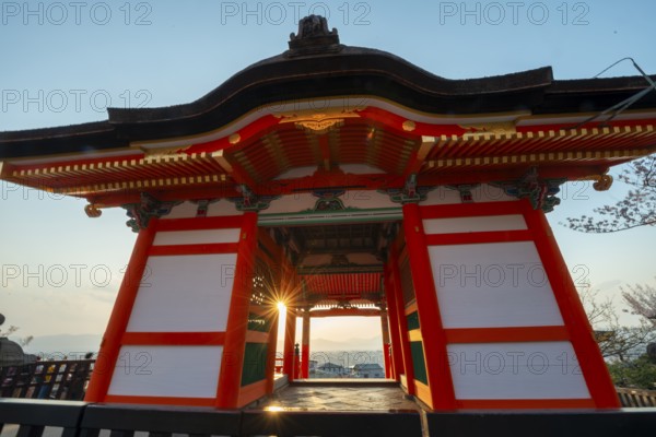 Sunset over the city with sun stars, view through the red Nishimon Gate, Kiyomizu-dera Temple, in