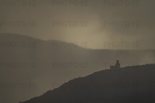 The structure is on a mountain. The sky is cloudy and sunlight is shining in the distance. The