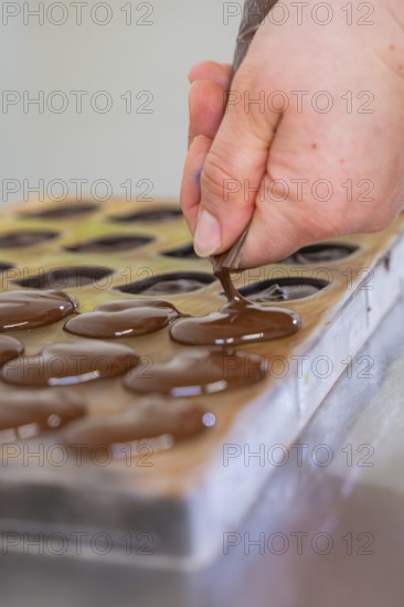 Hand fills chocolate into a mold on a table with a piping bag, vegan chocolates production,