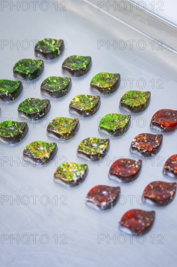 Chocolates in intense colors, decorated in leaf shapes, lie on a surface, vegan chocolates