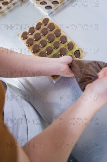 Hands fill liquid chocolate in a chocolate mold with a piping bag, vegan chocolates production,