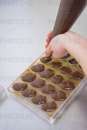 Hand with piping bag fills chocolate into molds on a work surface, vegan chocolates production,