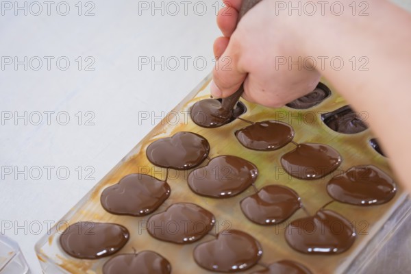 Hand with piping bag fills liquid chocolate in chocolate shape on a table, vegan chocolates