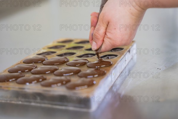 Hand fills chocolate into a chocolate mold lying on a table, vegan chocolates production,