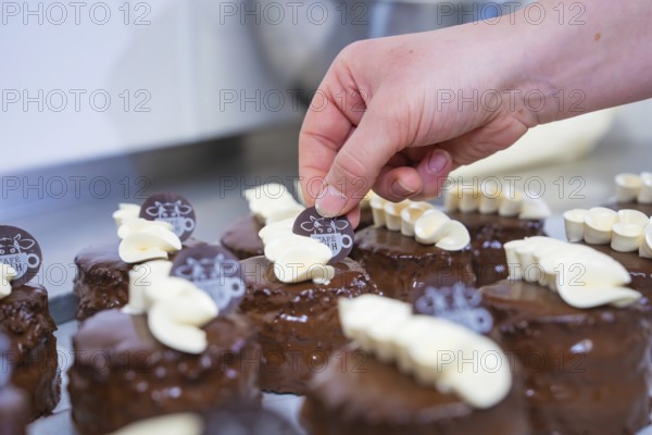Small chocolate cakes are decorated with café logo and white chocolate, Vegan Tartchen Production,