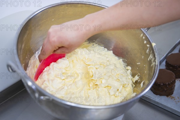 A hand stirs buttercream in a large metal bowl with dough spatula, vegan cake production,