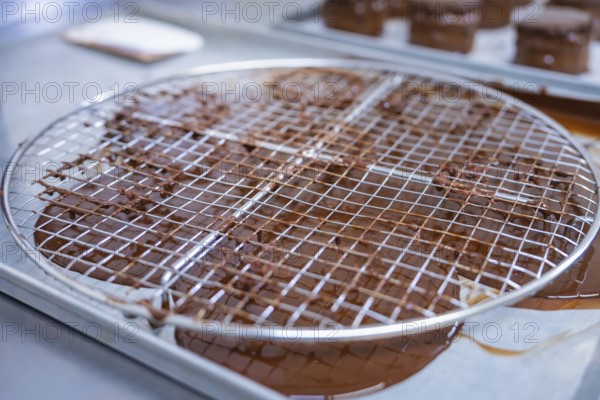 A metal grid with rotating chocolate grids, kitchen appliances in the background, vegan cake