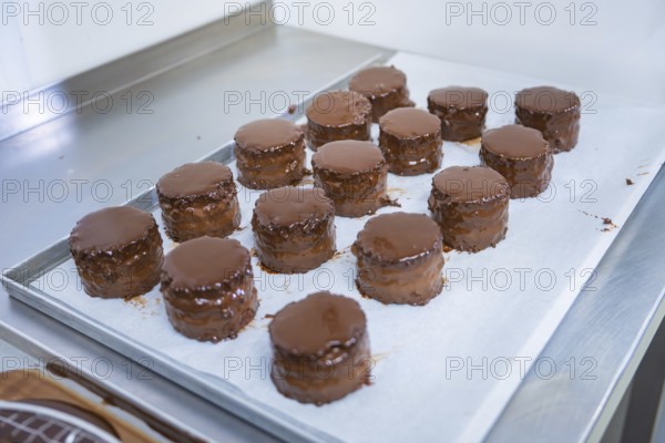 Round cakes with shiny chocolate glaze are arranged side by side on a sheet covered with paper,