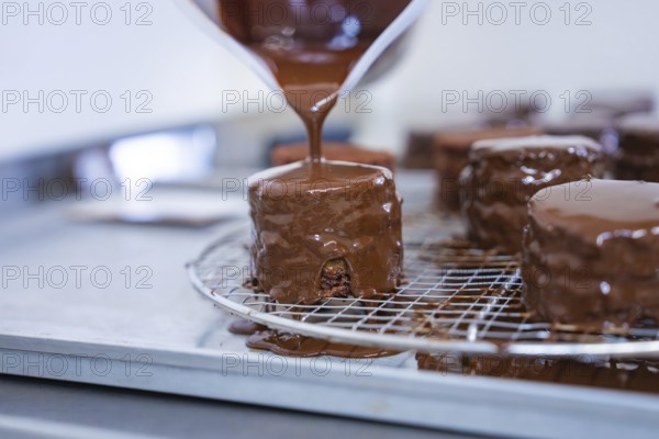 A pastry covered with liquid chocolate drips on a grid in a baking quality kitchen, vegan cake