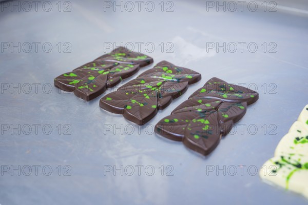 Three dark chocolate bars with green patterns on a table, vegan chocolate production, Haselstaller
