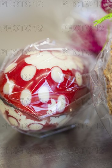 Red and white dotted Easter egg wrapped in plastic film on a metallic surface, Easter production of