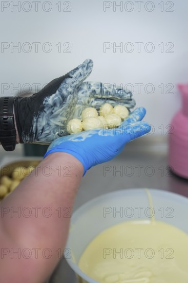 Person holding chocolates over a white bowl in a kitchen, chocolate quail eggs, Easter production,