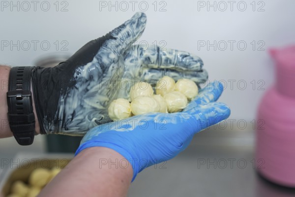 A hand in gloves holds chocolates over a bowl with pink and blue decoration, chocolate quail eggs,