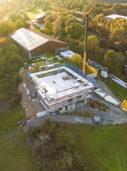 Aerial view of a construction site surrounded by forest and meadows with crane and building