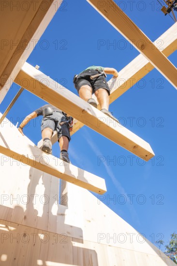 Two construction workers work on wooden scaffolding under a blue sky, Holzhausbau, Gechingen,