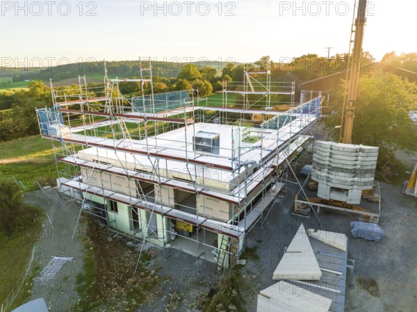 Building under construction with scaffolding in a rural area at sunset, timber house construction,