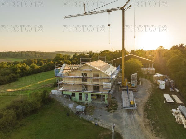 Building under construction, with a crane and scaffolding, in a green setting at sunset, timber