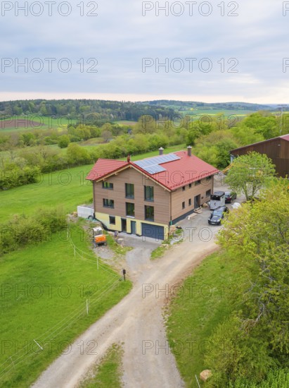 House with red roof and solar panel in rural area with green pastures and a road, Holzhausbau,