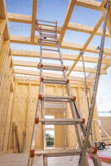 Interior view of a timber structure under construction, ladder leading upwards under blue sky,