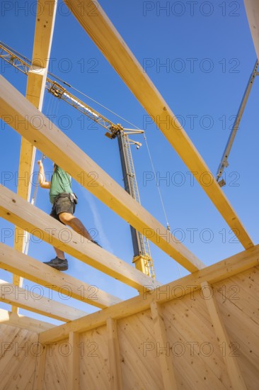 Construction worker balancing on wooden scaffolding under a clear sky, timber house construction,