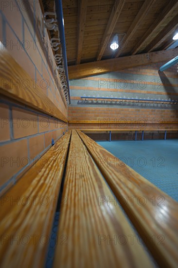 Long wooden bench on a brick wall with ceiling lights, Schlehengäu Sporthalle Gechingen, Calw