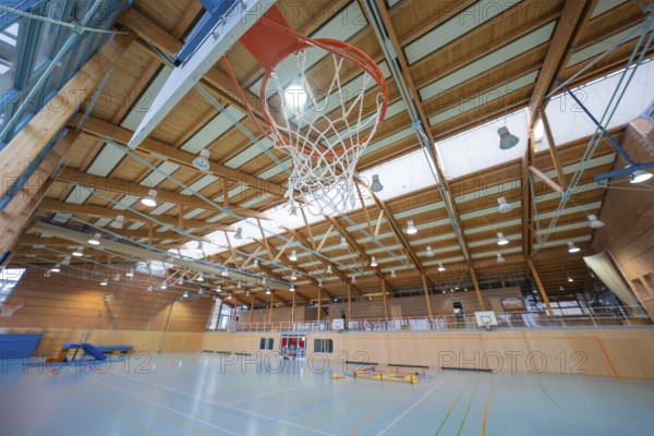Basketball hoop in a large sports hall with wooden structure and floor markings, Schlehengäu