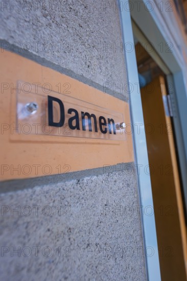 Close-up of a sign with the words' ladies' on a concrete wall next to a door, Schlehengäu