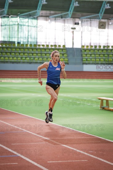 Woman running on a track in a stadium wearing a blue jersey, middle distance runner Katharina