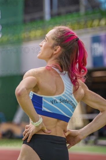 Sportswoman from behind in the stadium, sports outfit, pink hair tied in a braid, middle distance
