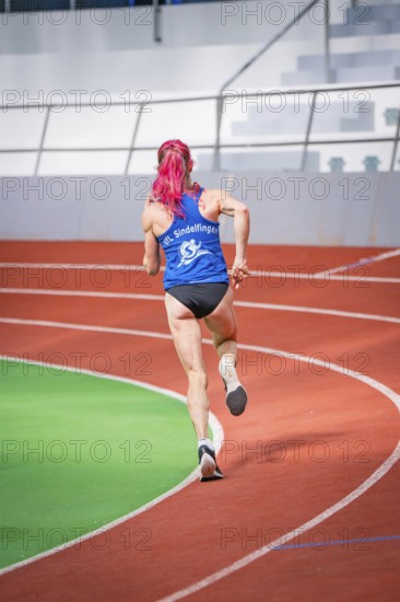 A sporty woman with pink hair dynamically runs along the curve in the stadium, middle distance