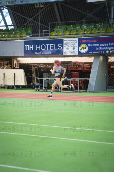 A sporty woman runs at high speed across the green track of a stadium with advertising, middle