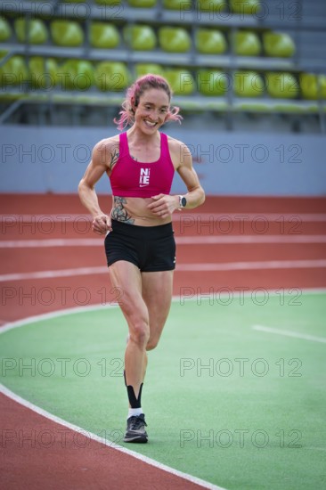 Determined, smiling woman running on an indoor track with visible enthusiasm, middle distance