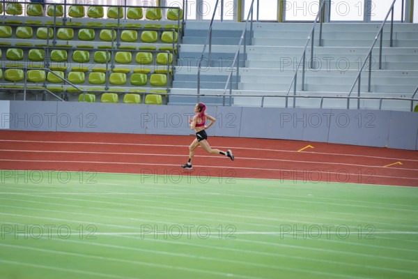 Woman running fast on a red track with strong concentration, middle distance runner Katharina
