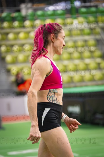 Side view of woman in sporty clothing, concentrated, with pink hair and tattoo, middle distance