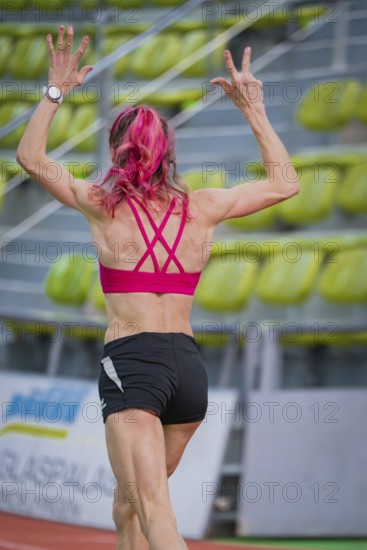 Sportswoman raises her arms while running on a track in a hall, middle distance runner Katharina