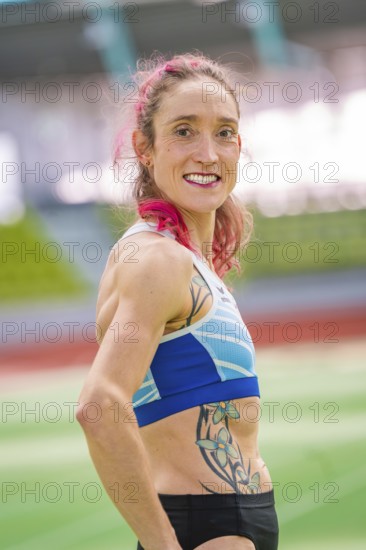 Sportswoman with blue sports outfit and tattoo in stadium, smiling with pink hair, middle distance