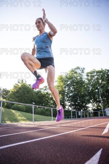 A sporty person jumps with momentum on the track in a blue outfit and pink shoes, middle distance