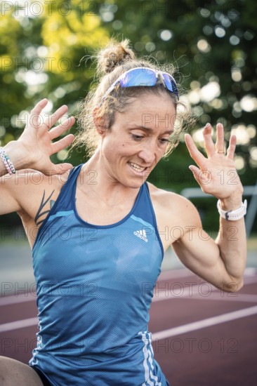 A happy runner in a blue sports outfit raises her hands with joy on the track, middle distance