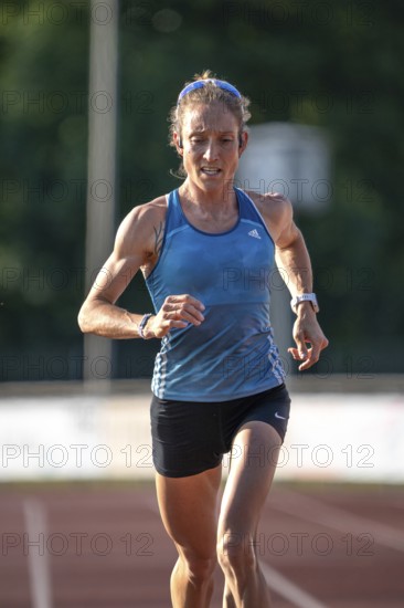 A focused runner on a racetrack wearing a blue sports outfit in sunshine, middle distance runner