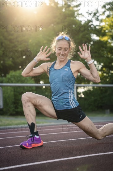 Joyful woman stretching with a smile on the track in sunshine, middle distance runner Katharina