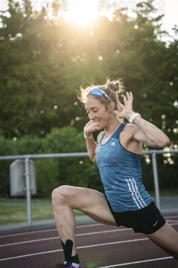 Woman stretching on the track at sunset, concentrated and energetic, middle distance runner