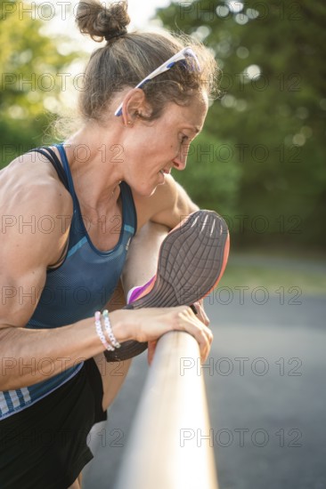 Woman stretches her leg over a barrier, concentrated in warm light and natural scenery, middle