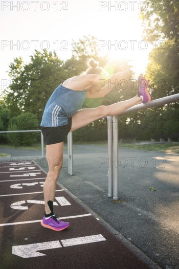 Woman doing stretching exercise on running track at sunrise, focus on flexibility, middle distance