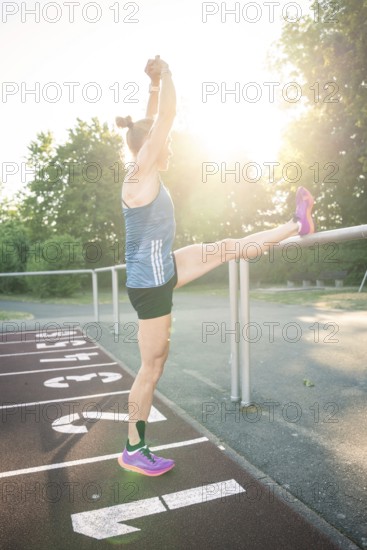 Woman stretches leg on track against bright sunshine, focus on stretching, middle distance runner