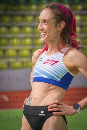 Smiling sportswoman with pink hair and tattoo, looks determined in the stadium, middle distance