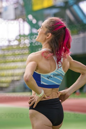 Female athlete with pink hair in the stadium, looking up. Determined atmosphere, middle distance